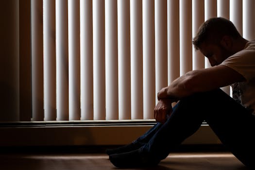 A depressed man sitting in closed room window blinds, conveying solitude and introspection.