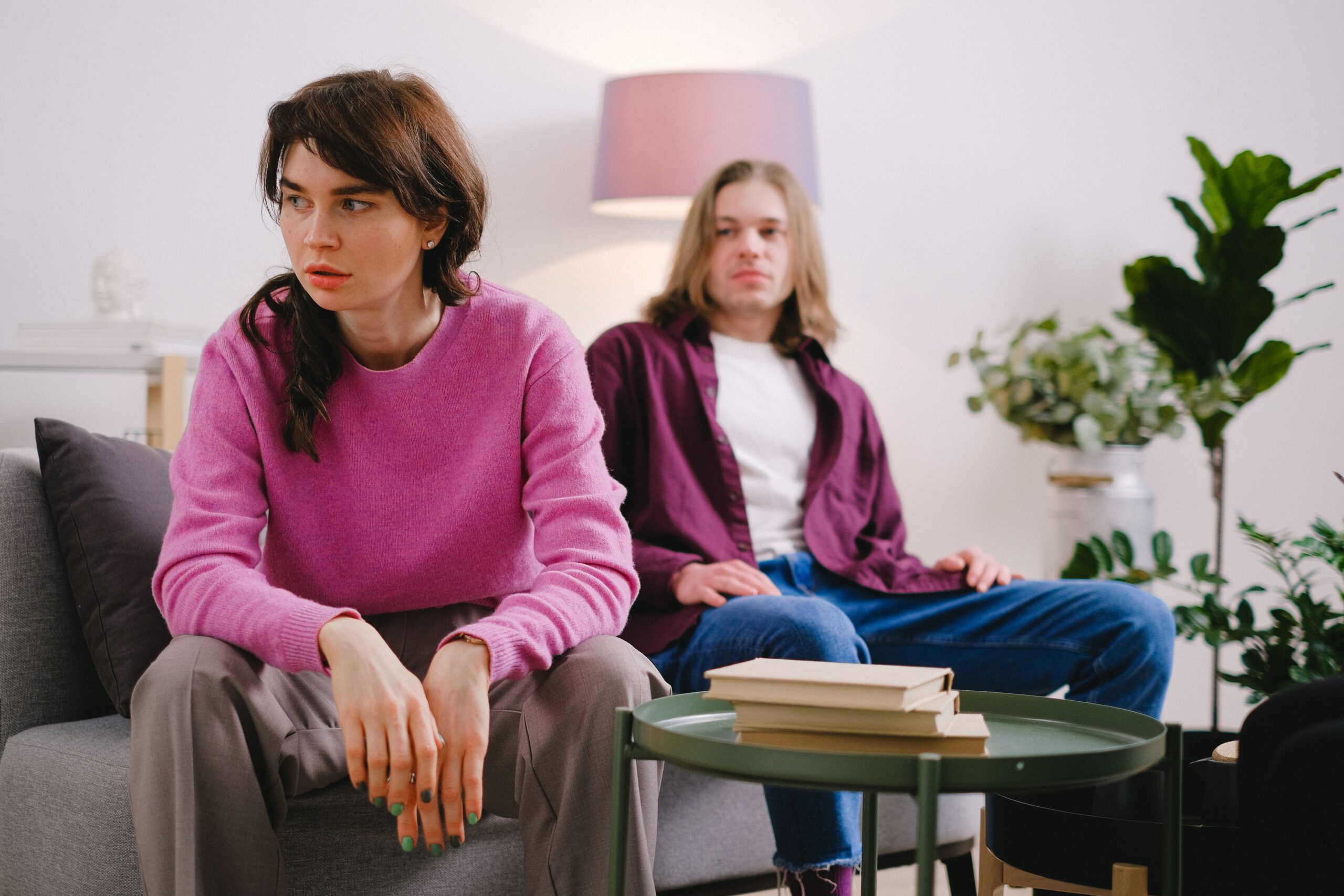 Couple experiencing relationship conflict at home, with a woman appearing emotionally distressed and a man sitting in the background during a tense discussion.